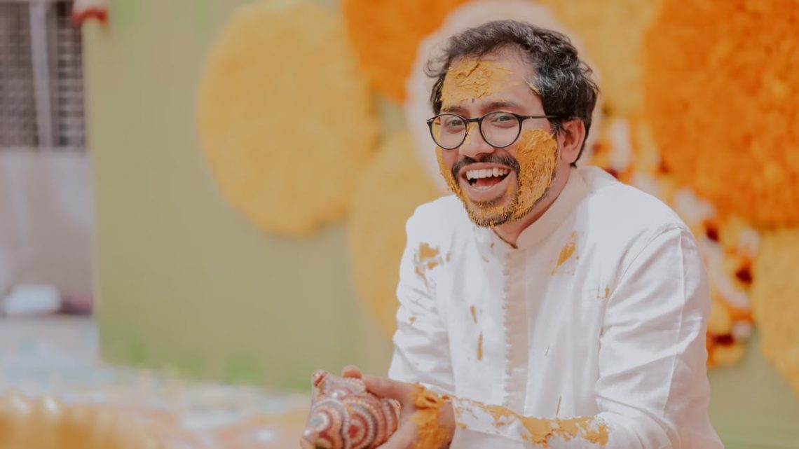 Happy Indian man laughing during traditional Haldi ceremony, covered in turmeric.