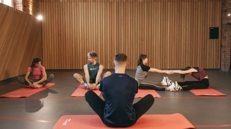 A group of adults practicing yoga and stretching on mats in a wooden panelled room.