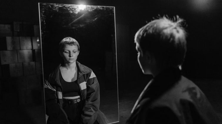 Black and white photo of woman with short hair reflecting in mirror, creating a contemplative mood.